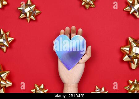 Futuristic image with a robot hand holding silver metal holographic heart on red drop with golden star bows. Robotic, ai, science, connection, technology, humanity concepts Stock Photo
