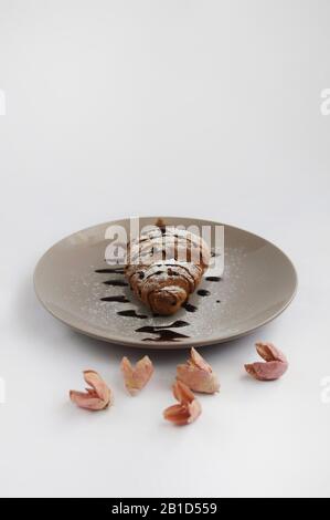 Croissant with chocolate and powdered sugar on the grey plate with flowers Stock Photo