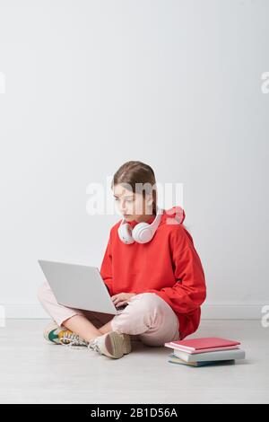 Curious schoolgirl with wireless headphones around neck performing online task on laptop Stock Photo