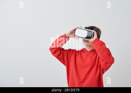 Girl in red hoodie using virtual reality goggles while watching movie in 3D against white background Stock Photo