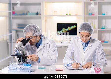 Busy multi-ethnic laboratory researchers in safety goggles sitting at desk and working with samples Stock Photo