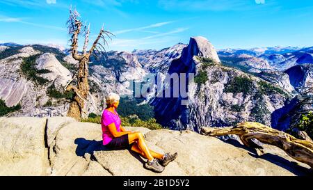 Active Senior Woman resting on a hike at Glacier Point in Yosemite National Park with the Half Dome in California, United Sates