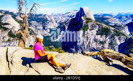 Active Senior Woman resting on a hike at Glacier Point in Yosemite National Park with the Half Dome in California, United Sates
