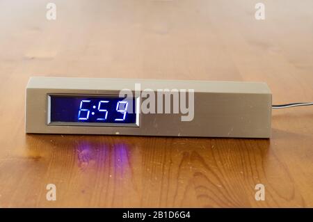 Digital alarm clock at 6:59 on wooden table Stock Photo