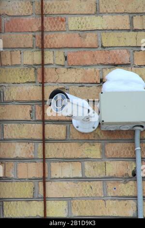 Surveillance camera mounted on brick wall of house. Security concept, tracking system, monitoring and control. Stock photo for web and print with empty space for text. Stock Photo