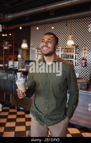 Handsome young afro-american man holding takeaway coffee mug standing in cafe Stock Photo