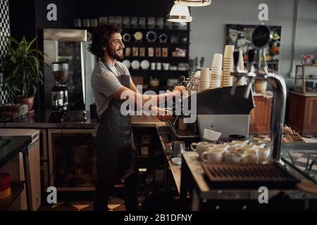 Cheerful caucasian coffee shop owner wearing apron preparing coffee using machine Stock Photo