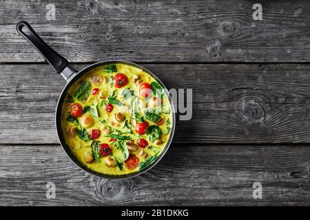 Yellow coconut and mushroom curry with champignons, fresh spinach, cherry tomatoes on a skillet on an old wooden background, horizontal orientation, c Stock Photo