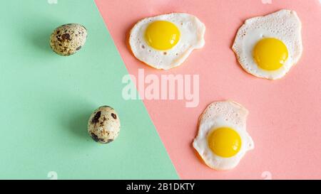 Three baked quail eggs on a pink background. And two whole eggs on a green background. Abstract, pop art. Stock Photo