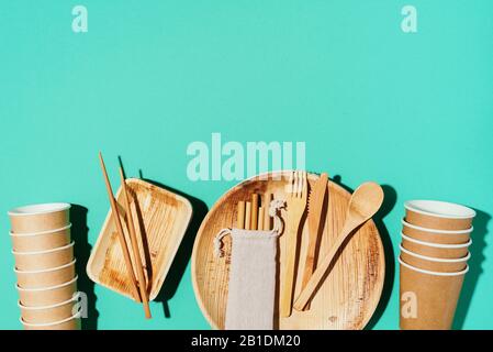 Bamboo plates, wooden spoon, fork, knife, craft paper cups on blue background. Disposable tableware from natural materials. Sustainable lifestyle concept. Eco-friendly disposable utensils. Stock Photo