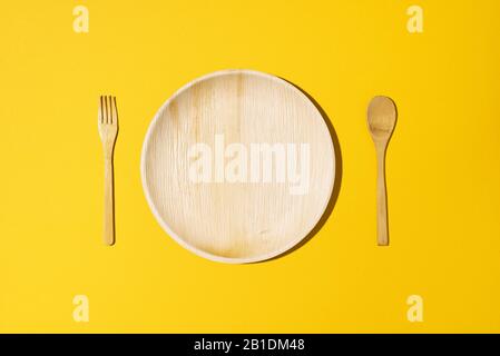 Disposable tableware from natural materials, wooden spoon, fork on yellow background. Eco-friendly sustainable lifestyle. Concept of bamboo, wooden or paper disposable tableware. Stock Photo
