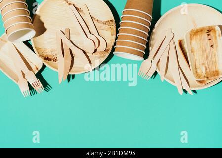 Disposable tableware from natural materials. Bamboo plates, wooden spoon, fork, knife, craft paper cups on blue background. Eco-friendly sustainable lifestyle. Eco-friendly disposable utensils. Stock Photo