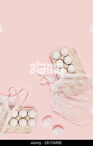 Happy Easter. White eggs with eyes in paper packaging and white mesh bags on pink background. Flat lay, top view, copy space. Stock Photo