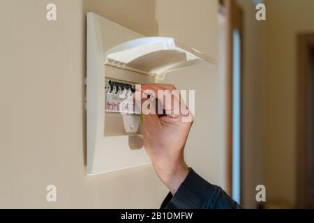 Hand switching power switch on a fusebox. Close up of electrician checking fuse box knob Stock Photo