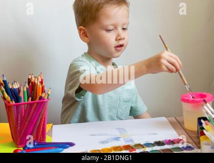 The child draws with a brush and paints on paper. Watercolor for drawing. Boy artist at school. Stock Photo