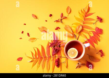 Autumn flat lay composition. Cup of tea, autumn bright leaves on yellow background. Top view. Flat lay. Autumn season concept. Stock Photo