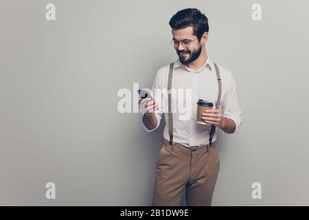 Positive marketer man student hold take-away mug beverage use smartphone cafeteria read social media news wear white formalwear white shirt pants Stock Photo