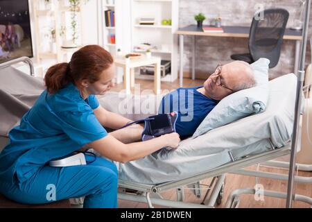 Female nurse doing a blood pressure check up on old man in nursing home. Stock Photo