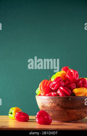 Colorful scotch bonnet chili peppers in wooden bowl over green background. Copy space