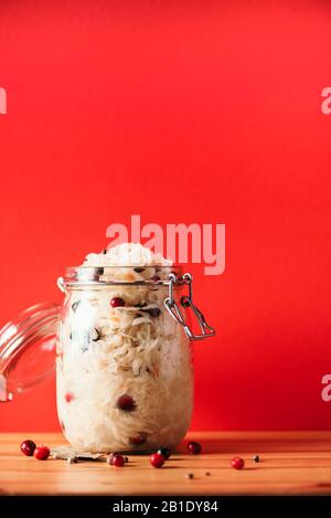 Fermented cabbage with cranberry in glass jar over wooden and red background. Probiotics food concept. Preserved vegetarian diet, homemade fermentation. Banner with copy space. Stock Photo