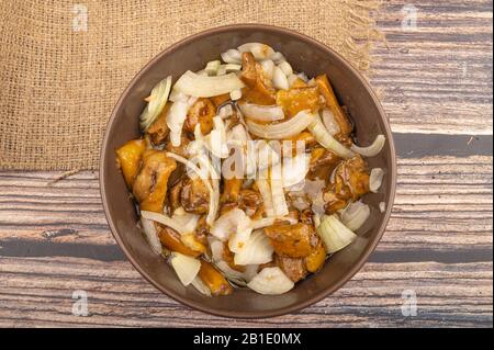 Salted mushrooms with onions in a ceramic bowl on a wooden background. Homemade preparations, rustic treats. Close up Stock Photo