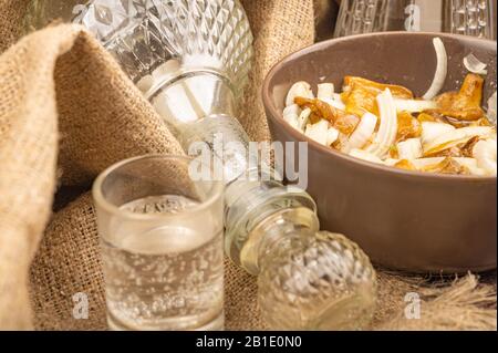 Salted mushrooms with onions in a ceramic bowl, a decanter and a glass of vodka on a background of rough homespun fabric. Homemade preparations, rusti Stock Photo