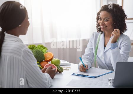 Smiling black woman talking to female patient, taking notes Stock Photo