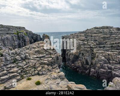 Amazing view over cliffs on San Pietro island , huge gray rocky strata rise high above the sea with emerald water,  natural travel destination with ma Stock Photo