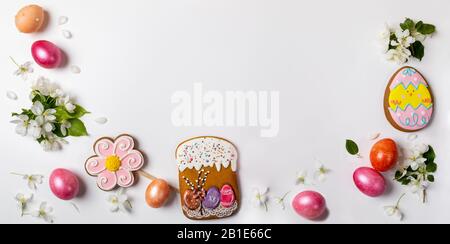 Easter festive banner. Arrangement as arc of gingerbreads as if Easter cake, flower and funny egg and colored eggs and white Apple tree twigs on white Stock Photo