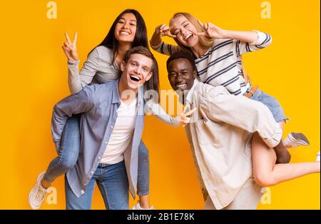 Two international teen couples having fun over yellow background Stock Photo