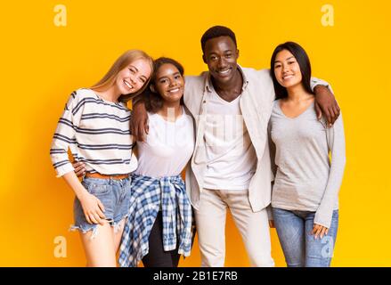 Positive multiethnic teenagers posing over yellow background Stock Photo
