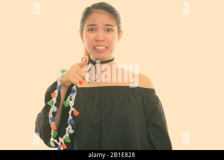 Studio shot of young Asian woman looking angry and pointing at camera Stock Photo