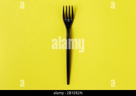 Black plastic fork on yellow background. plastic pollution Stock Photo