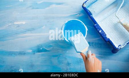 Hand Dips a brush in jar of blue paint Stock Photo