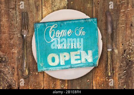 Vintage open sign on a dinner plate with fork and knive on an old wooden table Stock Photo