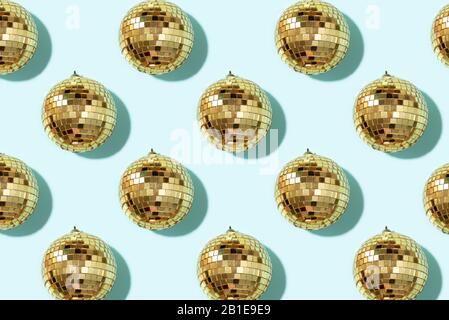 Creative Christmas pattern. Shiny gold disco balls over blue background. Flat lay, top view. New year baubles, star sparkles. Party time. Cristmas greeting card. Stock Photo