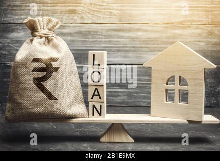 Miniature house and money bag with the word Loan on the scales. The concept of mortgage housing and real estate loans. Buy an apartment on credit. Lea Stock Photo