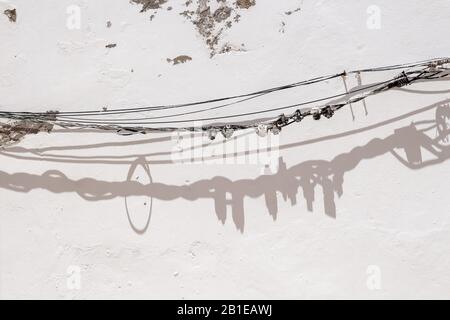 White older facade of a building. Bunch of cables along the wall with its shadow in a strong sunlight. Estoi, Portugal. Stock Photo