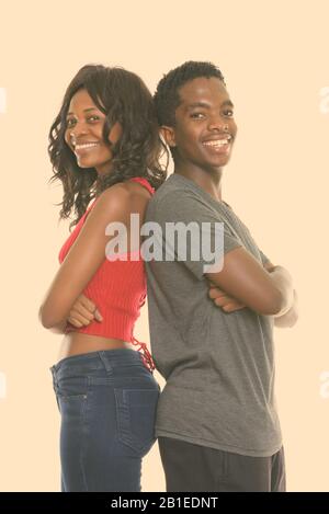 Studio shot of happy black African sister and brother smiling with arms crossed and back to back Stock Photo