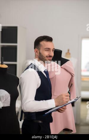 Male tailor in a black vest smiling, thinking, making notes Stock Photo