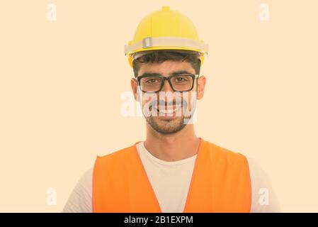 Studio shot of young happy Persian man construction worker smiling while wearing eyeglasses Stock Photo