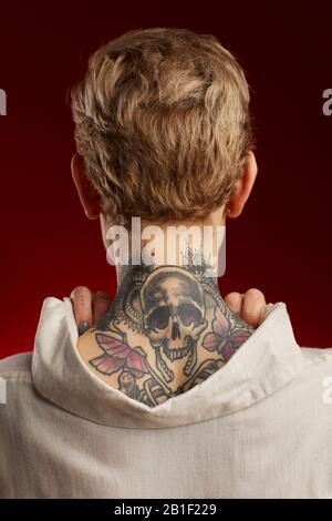 Back view of neck tattoo featuring scull and butterflies on short haired young woman posing against red background Stock Photo