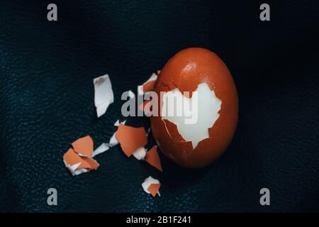 Cracked hard boiled brown egg with heart shaped shell on black leather background. Minimal Easter holiday concept. Stock Photo