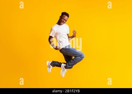 Happy excited young black man jumping over yellow Stock Photo