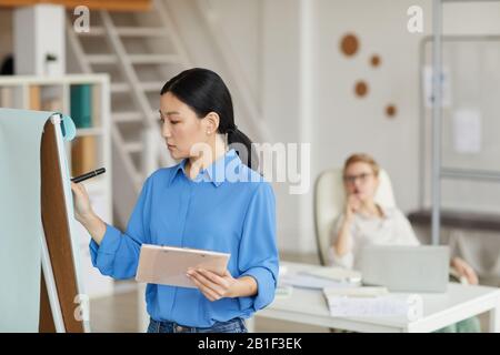 Side view portrait of Asian businesswoman writing on whiteboard while planning project in office, copy space Stock Photo