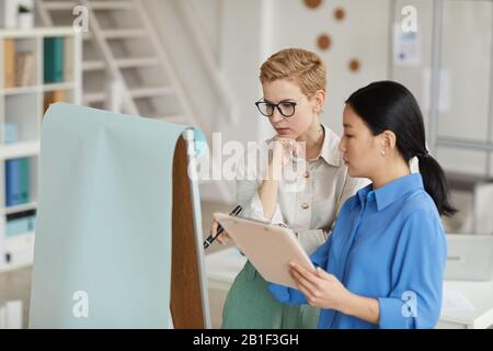 Side view portrait of of two businesswomen writing on whiteboard while planning project in office, copy space Stock Photo