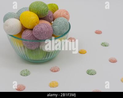 Glass bowl filled with string decorated Easter eggs with little candies on white background, perfect decor for the holiday, festive and pastel! Stock Photo