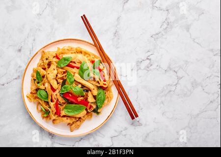 Thai Drunken Noodles or Pad Kee Mao at white marble background. Drunken Noodles is thai cuisine dish with Rice Noodles, Chicken meat, Basil, sauces an Stock Photo