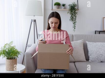 Young woman unpacking order and checking with cellphone Stock Photo
