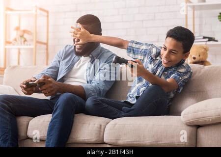 Afro dad and son with joysticks playing video games at home Stock Photo